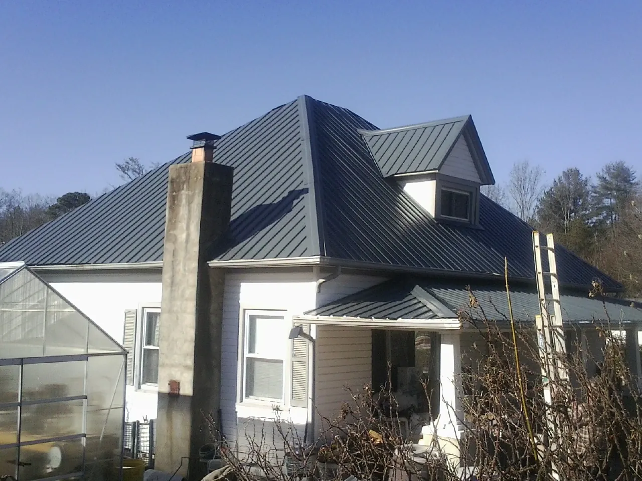Dark blue standing seam metal roof on a white farmhouse with dormer — Slate & Tile Roof Repair by Roofing Brothers in Central