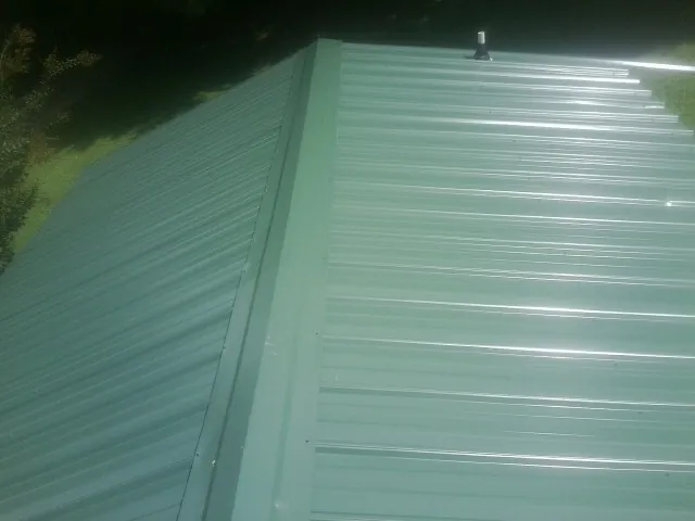 New green metal panels meeting at the ridge of a roof — Flat Roof Repair work by our crew in Central