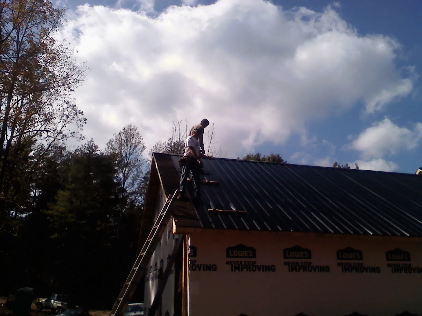 Roofer fastening dark metal panels high against a cloudy sky, from a Roof Inspection job in Central